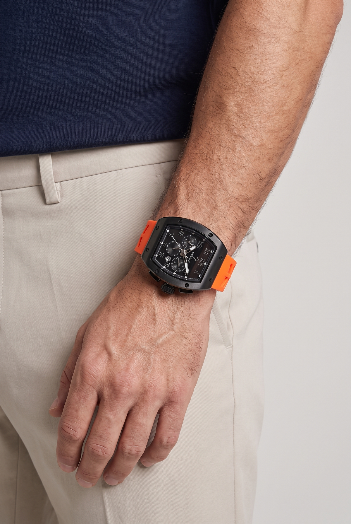 Astos Millionaire 2.0 Black met oranje band om de pols, model in navy shirt, studio