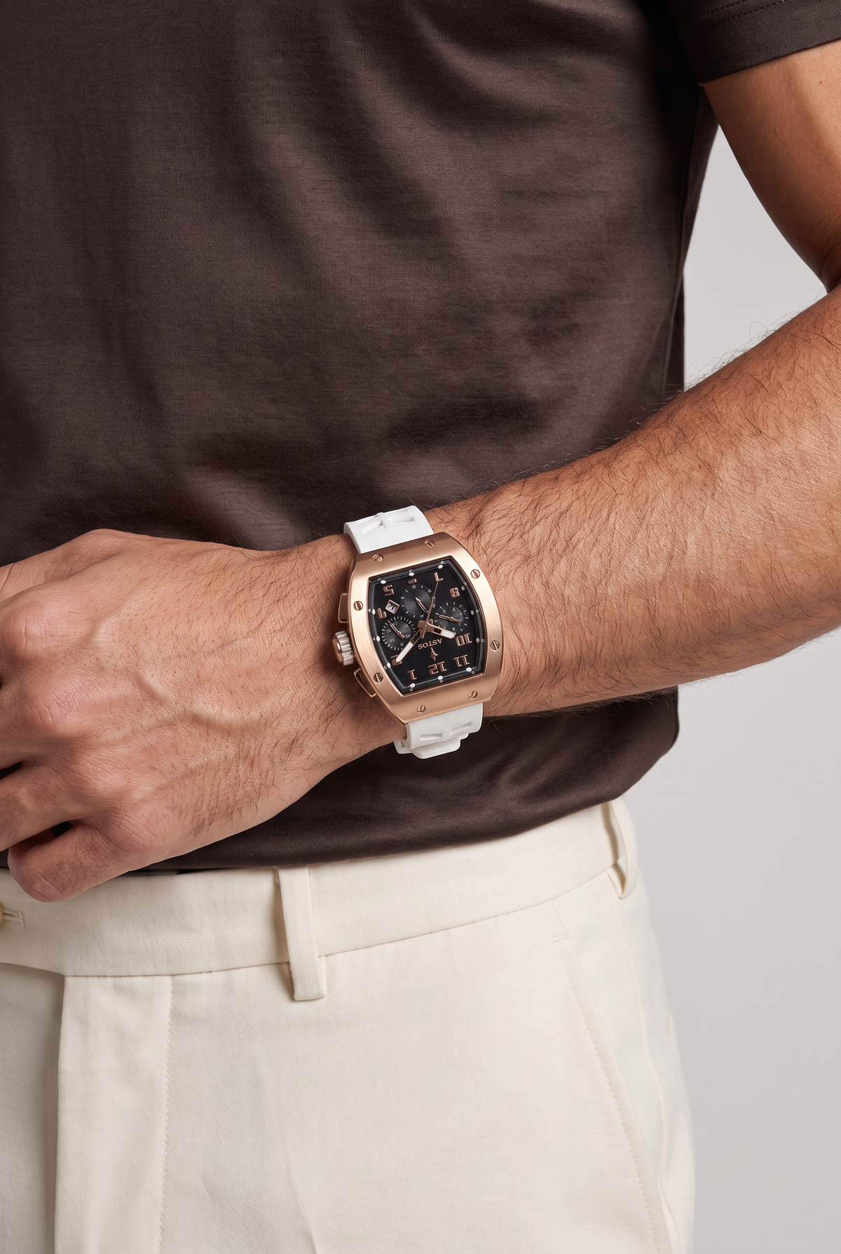 Astos Millionaire 2.0 Rose Gold met witte band om de pols, model in bruin shirt, studio